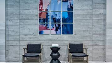 A modern interior with two wooden chairs and a black table, a large abstract painting on the wall, and a grey wooden panel backdrop.