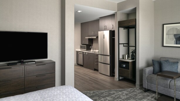 Une chambre d’hôtel moderne dotée d’un grand lit, d’une télévision à écran plat, d’une kitchenette et d’un coin salon avec un canapé et une petite table.