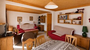 Une pièce chaleureuse avec un plafond en bois, un canapé, une table à manger et une bibliothèque.