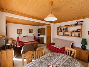 Ein gemütliches Zimmer mit Holzbalkendecke, einer Couch, einem Esstisch und einem Bücherregal.