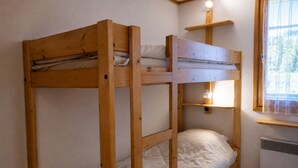 A bunk bed with a wooden frame, a bedside table, a shelf with a lamp, and a window with a view. - Méribel apartment perfect for skiers with balcony and parking (Méribel)
