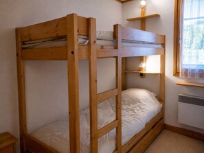 A bunk bed with a wooden frame, a bedside table, a shelf with a lamp, and a window with a view. - Méribel apartment perfect for skiers with balcony and parking (Méribel)