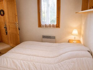 Une chambre à coucher avec un lit, une fenêtre ornée de rideaux en dentelle, une armoire en bois et une lampe de chevet.