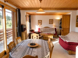 Una habitación acogedora con techo de madera, una mesa redonda de comedor, una cama con cubrecama rojo con lunares y un televisor sobre un mueble de madera.