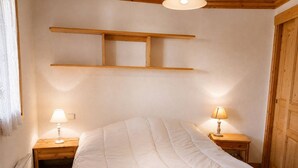 Une chambre à coucher avec un lit, deux tables de chevet avec des lampes, une étagère en bois au-dessus du lit, un radiateur et une porte en bois.