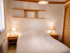 Ein Schlafzimmer mit einem Bett, zwei Nachttischen mit Lampen, einem Holzregal über dem Bett, einer Heizung und einer Holztür.