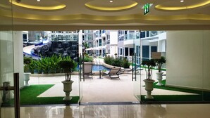 Vestíbulo de hotel con entrada de vidrio, zona de piscina con sillones de descanso y una cascada.