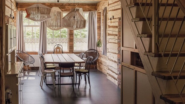 Een ruime eethoek met een houten tafel en stoelen, een trap en een uitzicht op groen door grote ramen.