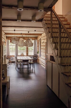 A spacious dining area with a wooden table and chairs, a staircase, and a view of greenery through large windows. - Daj Spokój - slow apartments (Szczyrk)