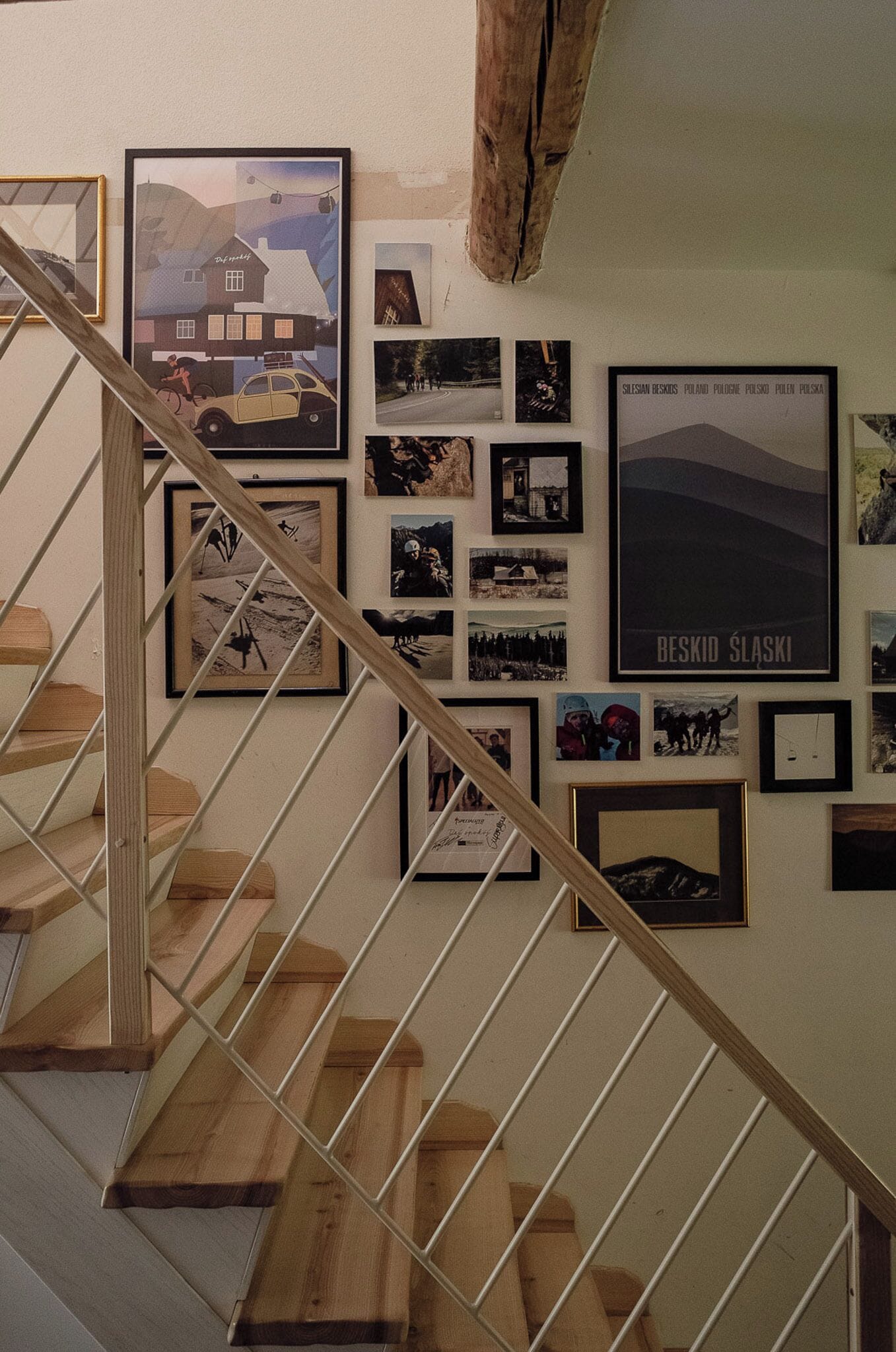 A staircase with wooden steps and white railings, leading to a wall adorned with various framed pictures and posters.
