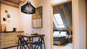 Cocina compacta con armarios de madera, una mesa de comedor y sillas negras. Un cuadro grande y una lámpara colgante decoran la pared.