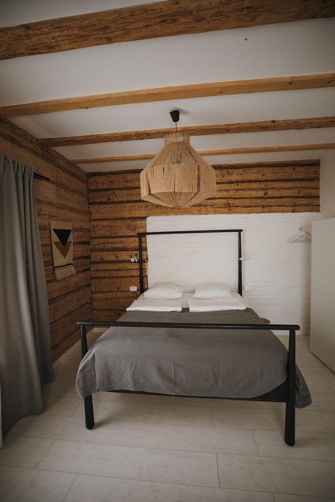 Un dormitorio con cama, paredes de madera, un muro de ladrillo blanco, una lámpara colgante y una cortina.