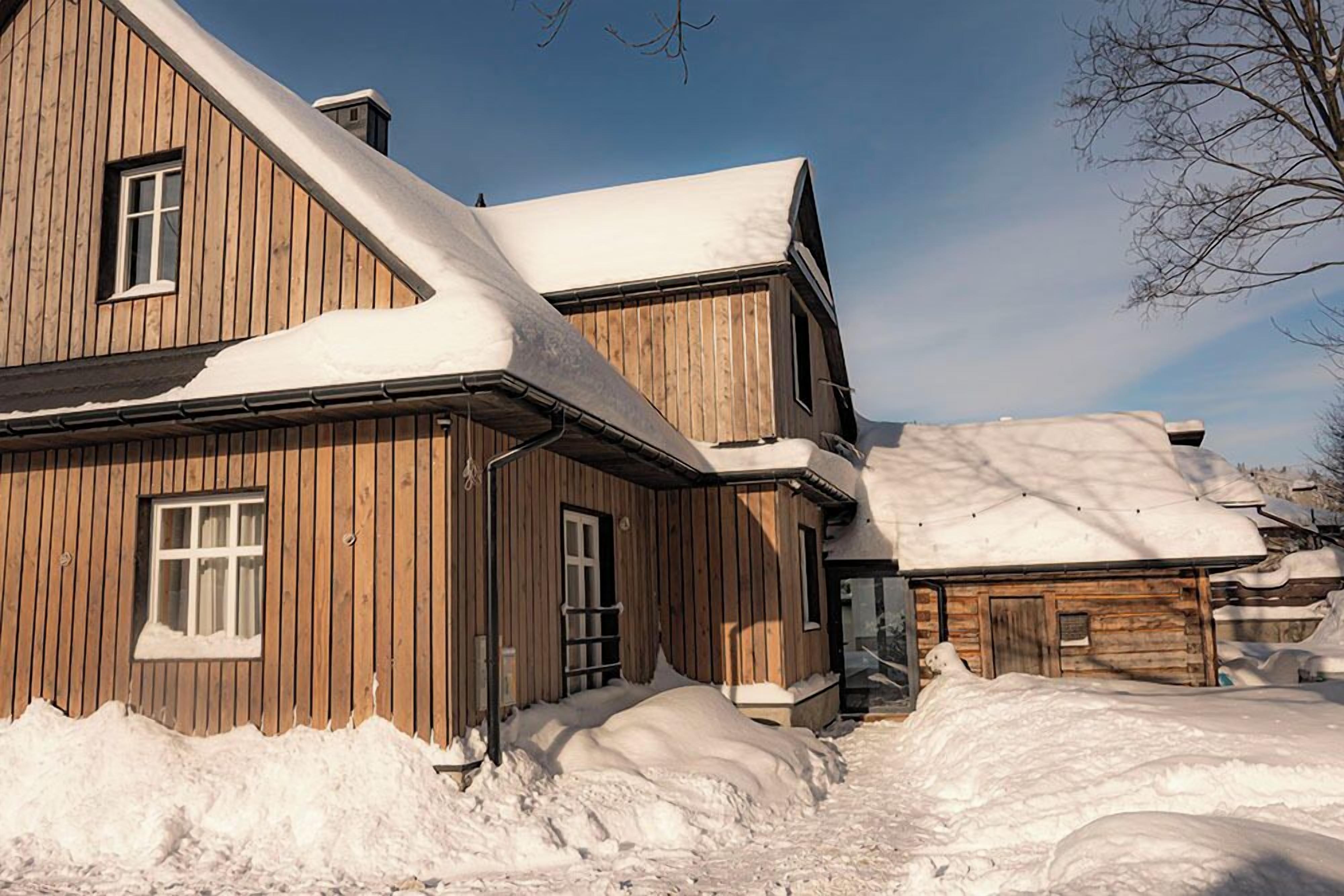 A wooden cabin with a sloped roof covered in snow, surrounded by snowbanks.