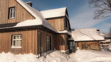 A wooden cabin with a sloped roof covered in snow, surrounded by snowbanks.