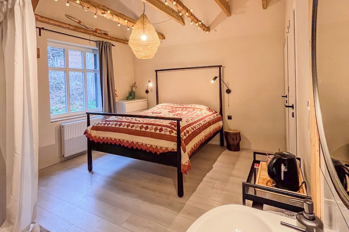 A bedroom with a bed, a large window, a hanging light fixture, a mirror, and a white sink.