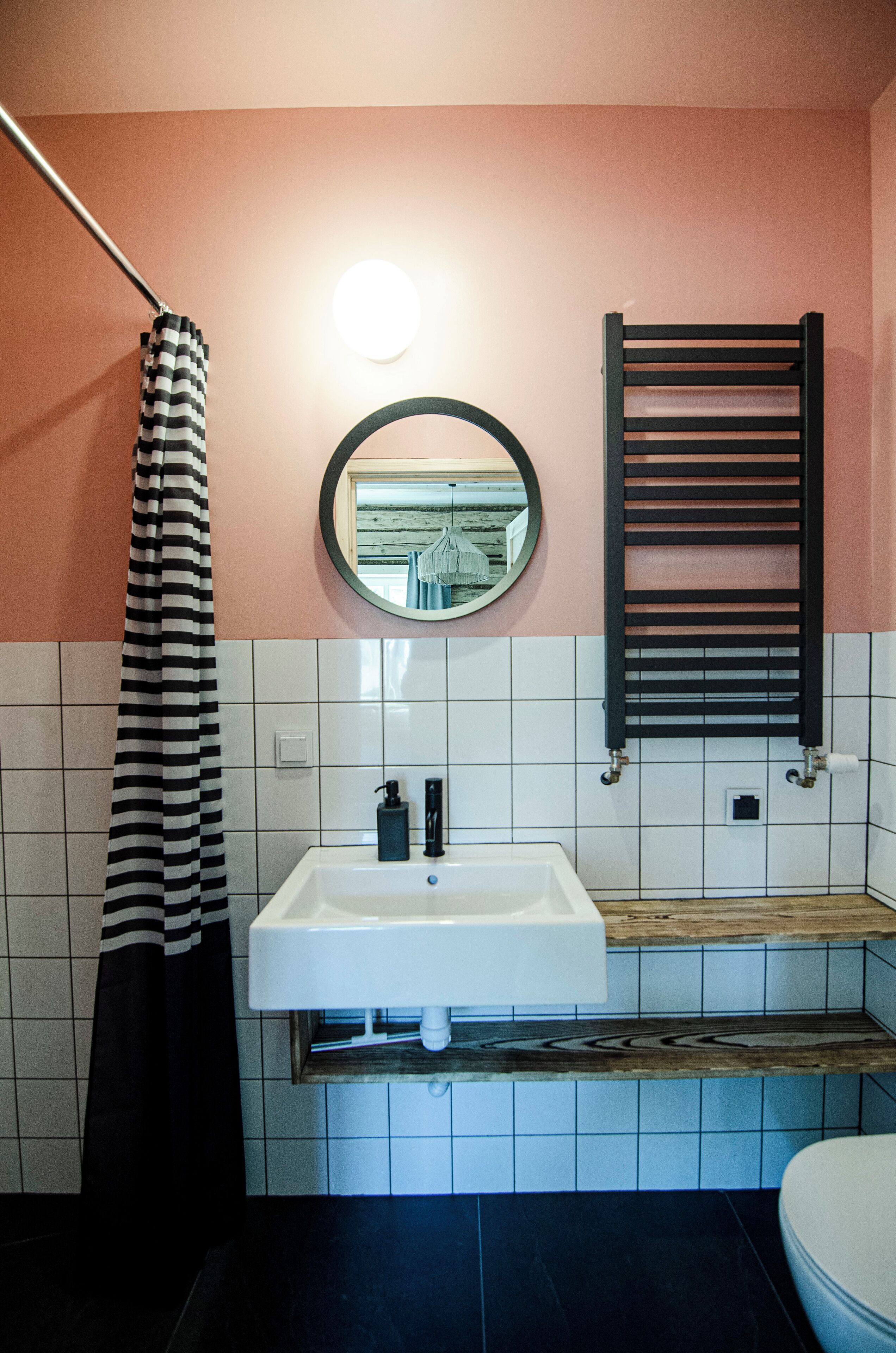 A bathroom with a white sink, a black and white striped shower curtain, a round mirror, and a black towel rack.