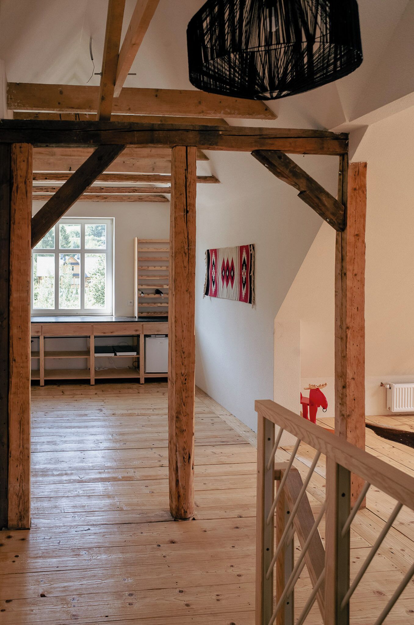 A spacious attic room with exposed wooden beams, a large window, and a view of the outdoors.