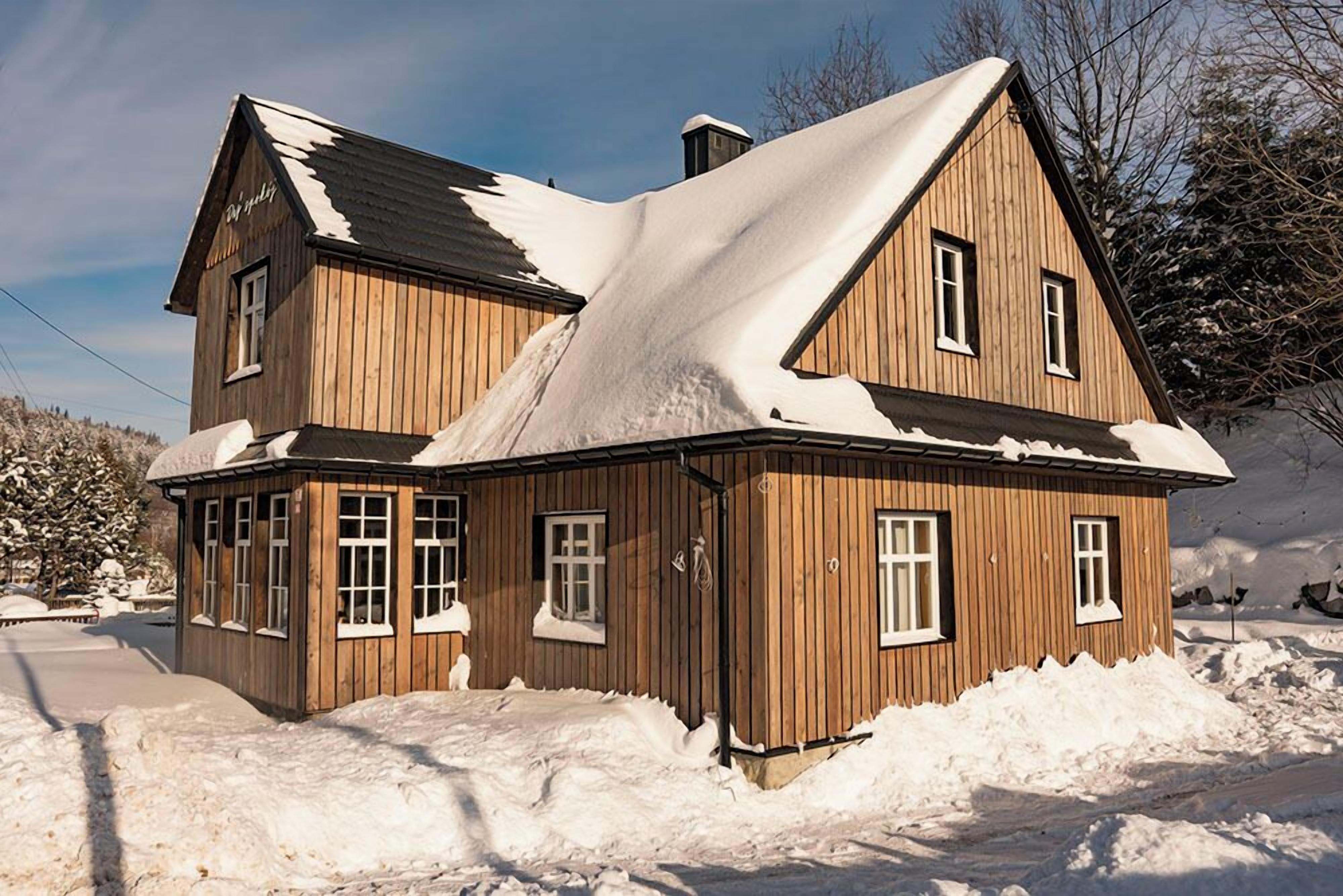 A wooden house with a steep roof, surrounded by snow.