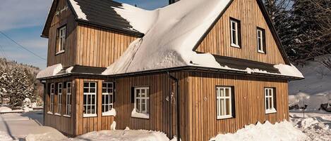 A wooden house with a steep roof, surrounded by snow.