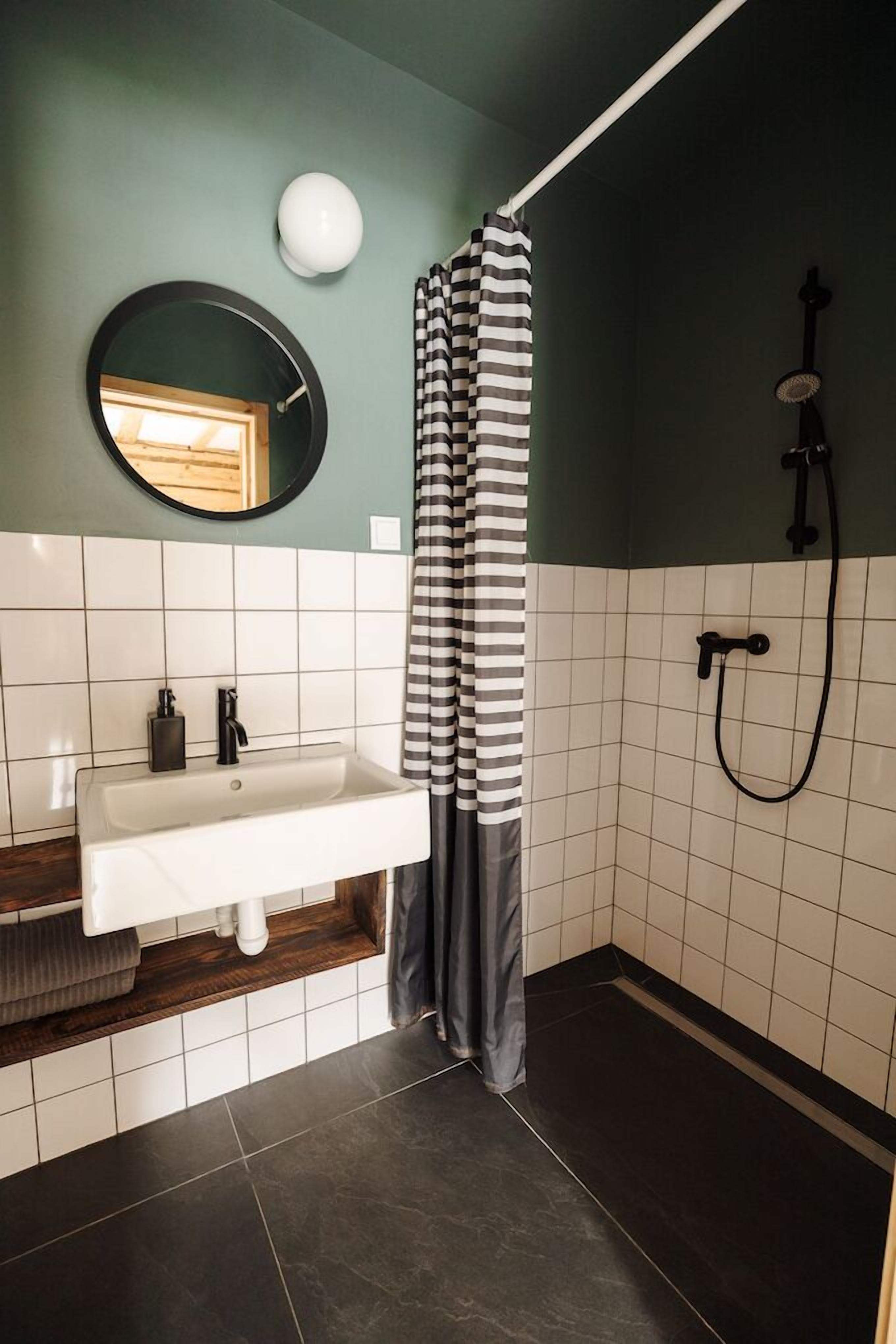 Une salle de bain avec un lavabo blanc, un miroir rond, une douche avec un tuyau noir et un rideau de douche à rayures.
