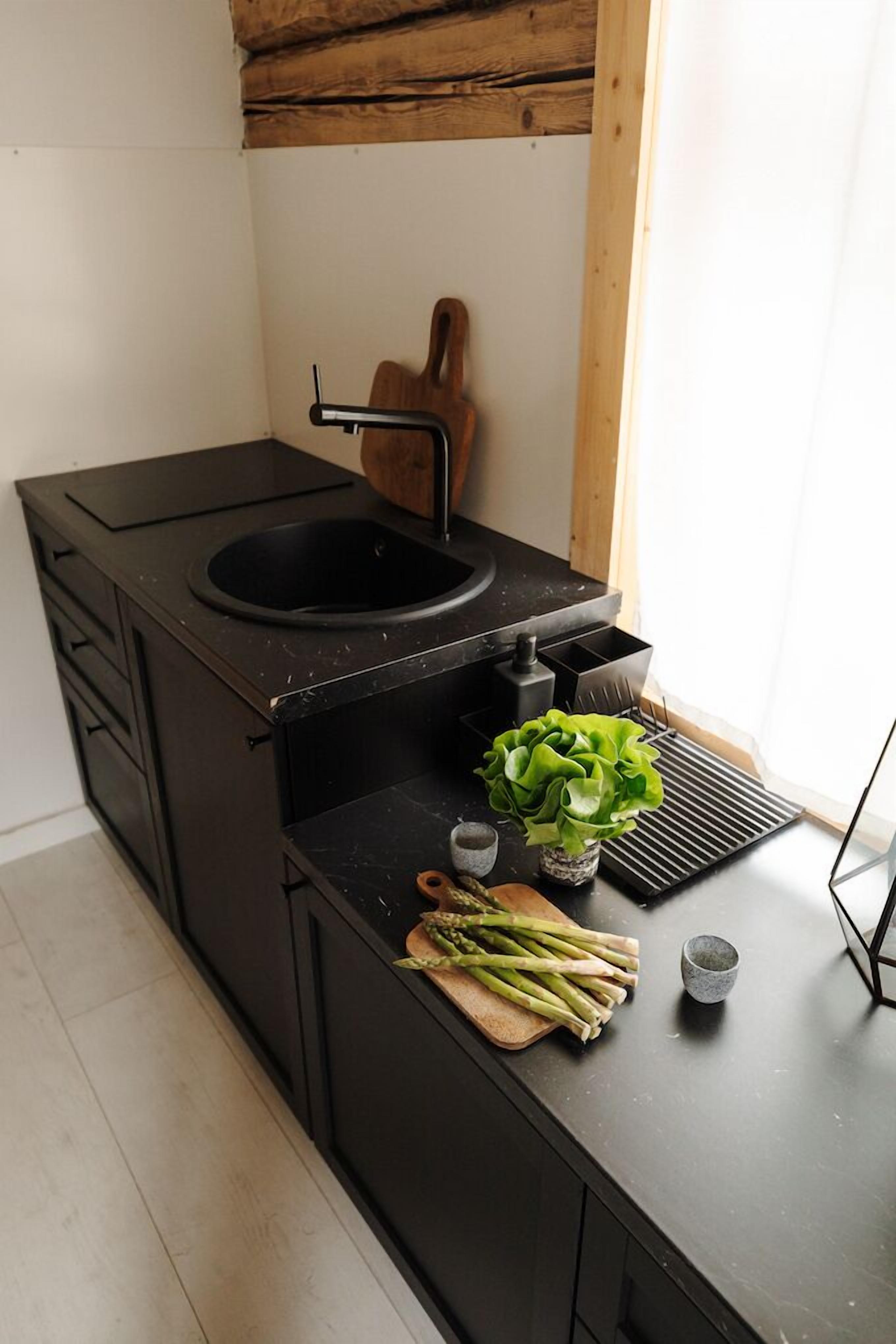 A compact kitchen with a black countertop, a sink, a wooden cutting board with vegetables, and a small potted plant.