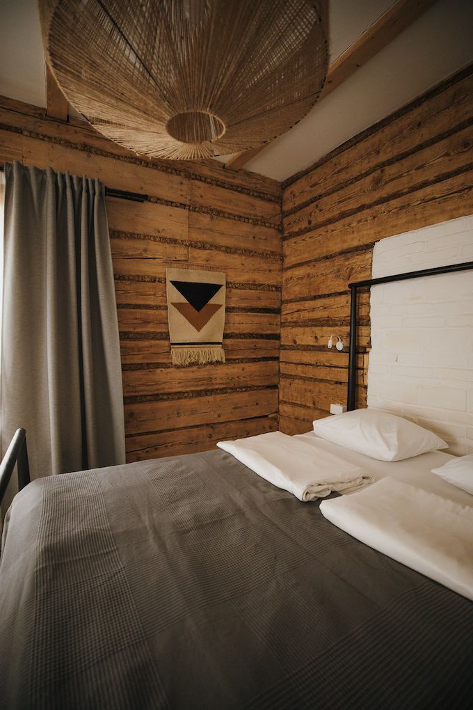 Een kamer met houten lambrisering, een bed, een geweven plafondlamp en een decoratief object aan de wand.