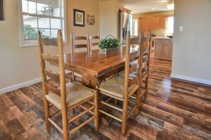 Un coin repas avec une table et des chaises en bois, une fenêtre et une cuisine en arrière-plan.