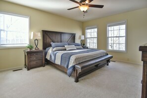 A bedroom with a bed, two bedside tables with lamps, a ceiling fan, and large windows.