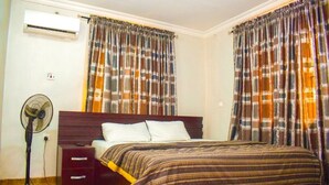 Un dormitorio con cama, ventilador, mesita de noche y cortinas.