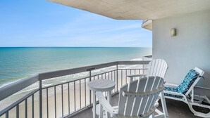 Un balcon avec vue sur l’océan, des fauteuils Adirondack blancs et une petite table.