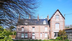 Un grand bâtiment en briques de deux étages, doté de nombreuses fenêtres et d’une tour d’angle imposante.