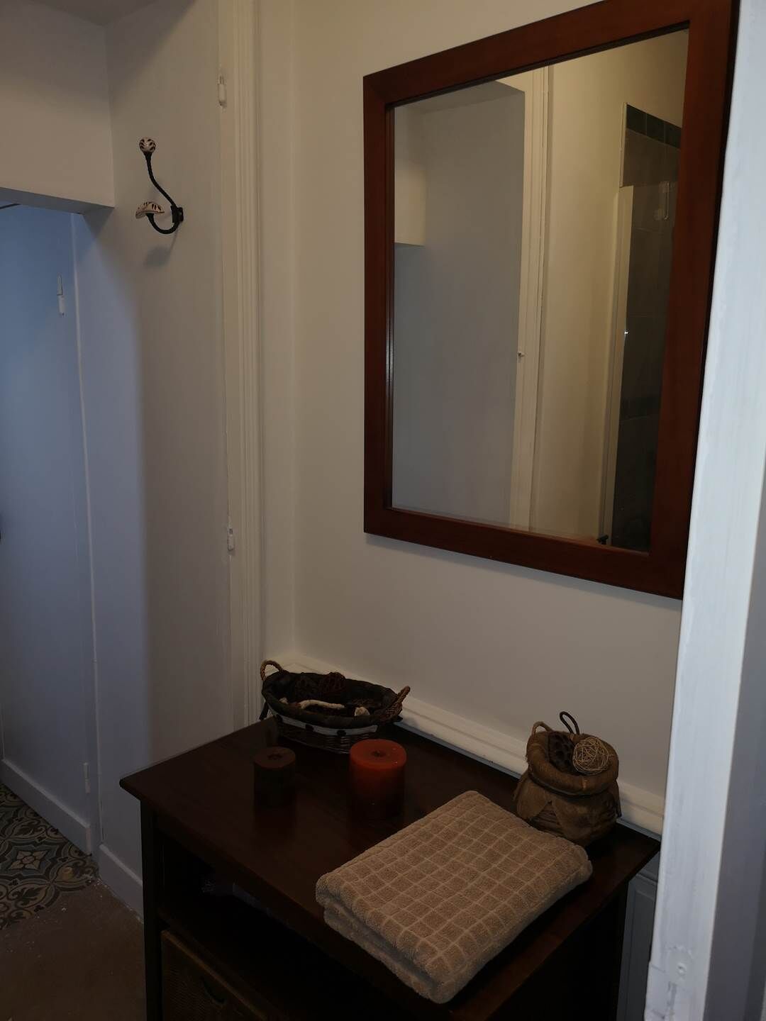 Un baño pequeño con tocador de madera, un espejo, una cesta y una vela.