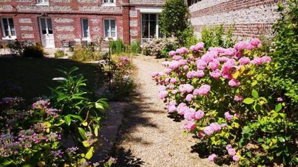 Un chemin de jardin mène à un bâtiment en briques avec une porte blanche.