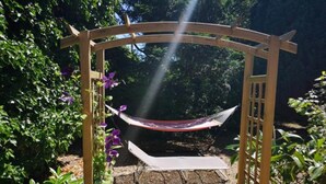 Un hamac suspendu sous une arche en bois, dans un jardin.