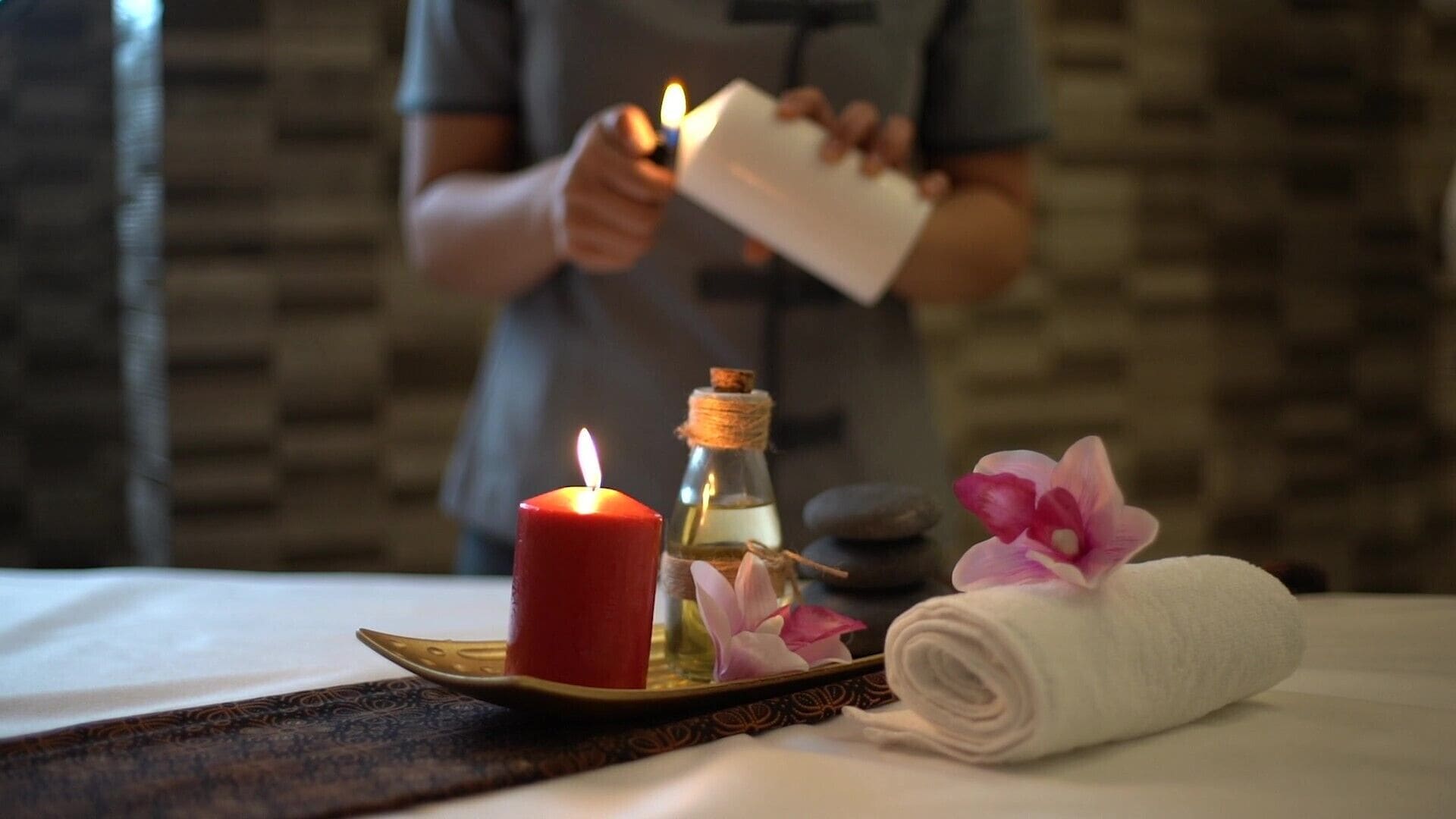 A candle, a bottle, and a rolled towel on a tray.