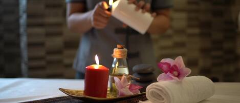 A candle, a bottle, and a rolled towel on a tray.