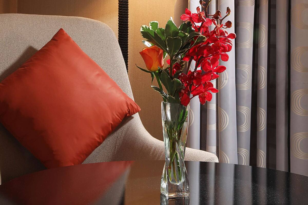 Une chambre d’hôtel avec une lampe, une chaise dotée d’un coussin rouge et un vase rempli de fleurs.