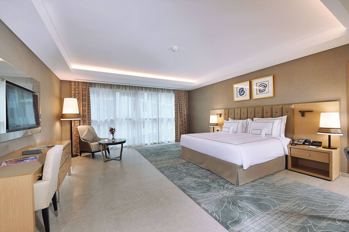 Une chambre d’hôtel avec un lit, un bureau, une chaise et une grande fenêtre avec des rideaux.