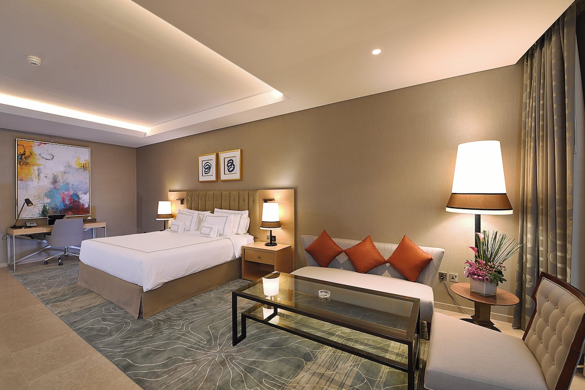 Une chambre d’hôtel comprenant un lit, des tables de chevet, un bureau, une chaise et une table basse en verre.