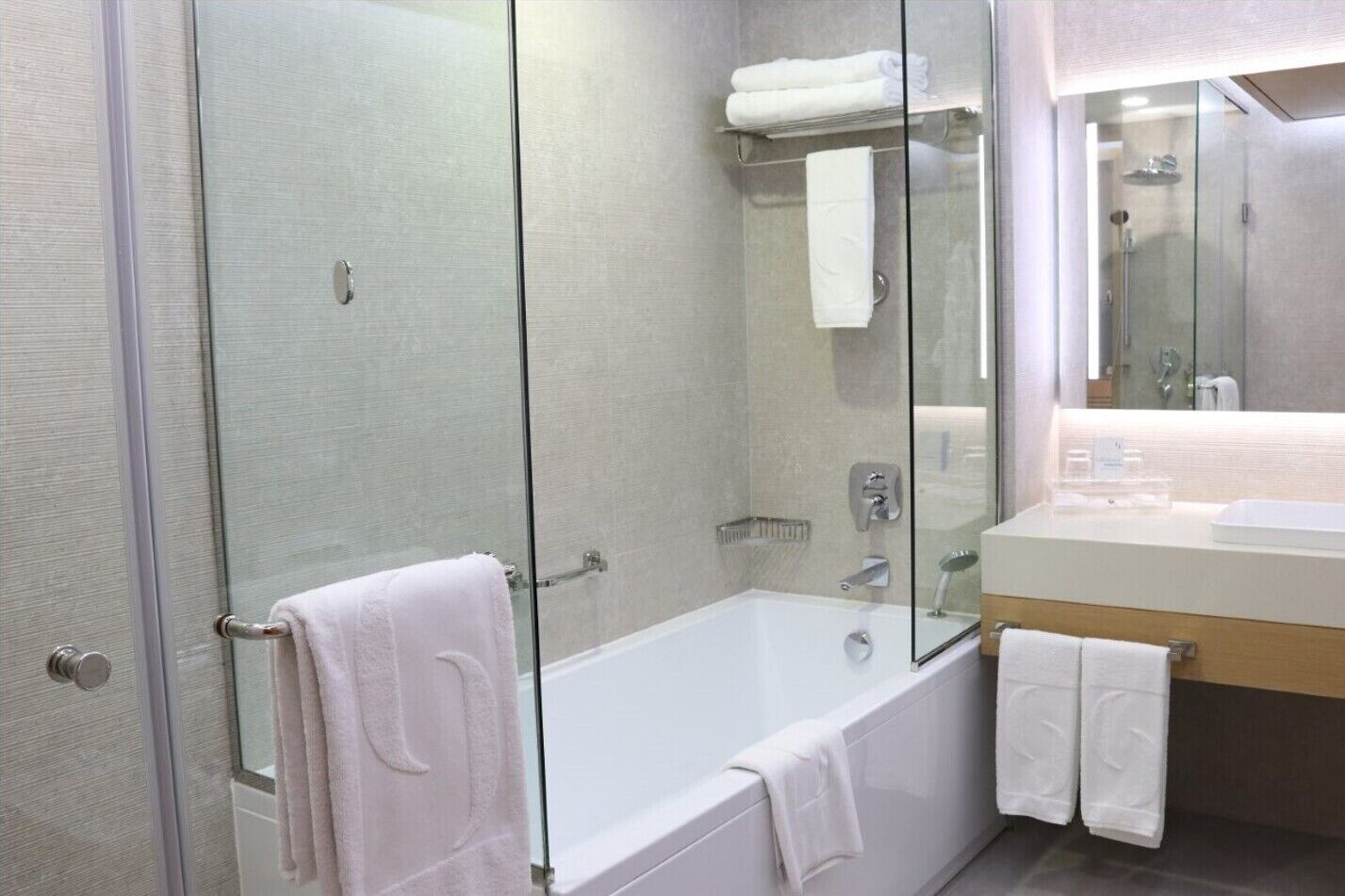 Een moderne badkamer met een douchecabine van glas, een wit bad en een wastafel met spiegel.