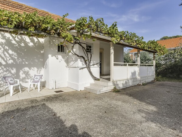 A white house with a covered porch, a small garden, and two white plastic chairs. - Cozy Beach House: Steps from Center, 400m to Ocean, Sleeps 6 (Biscarrosse Plage)