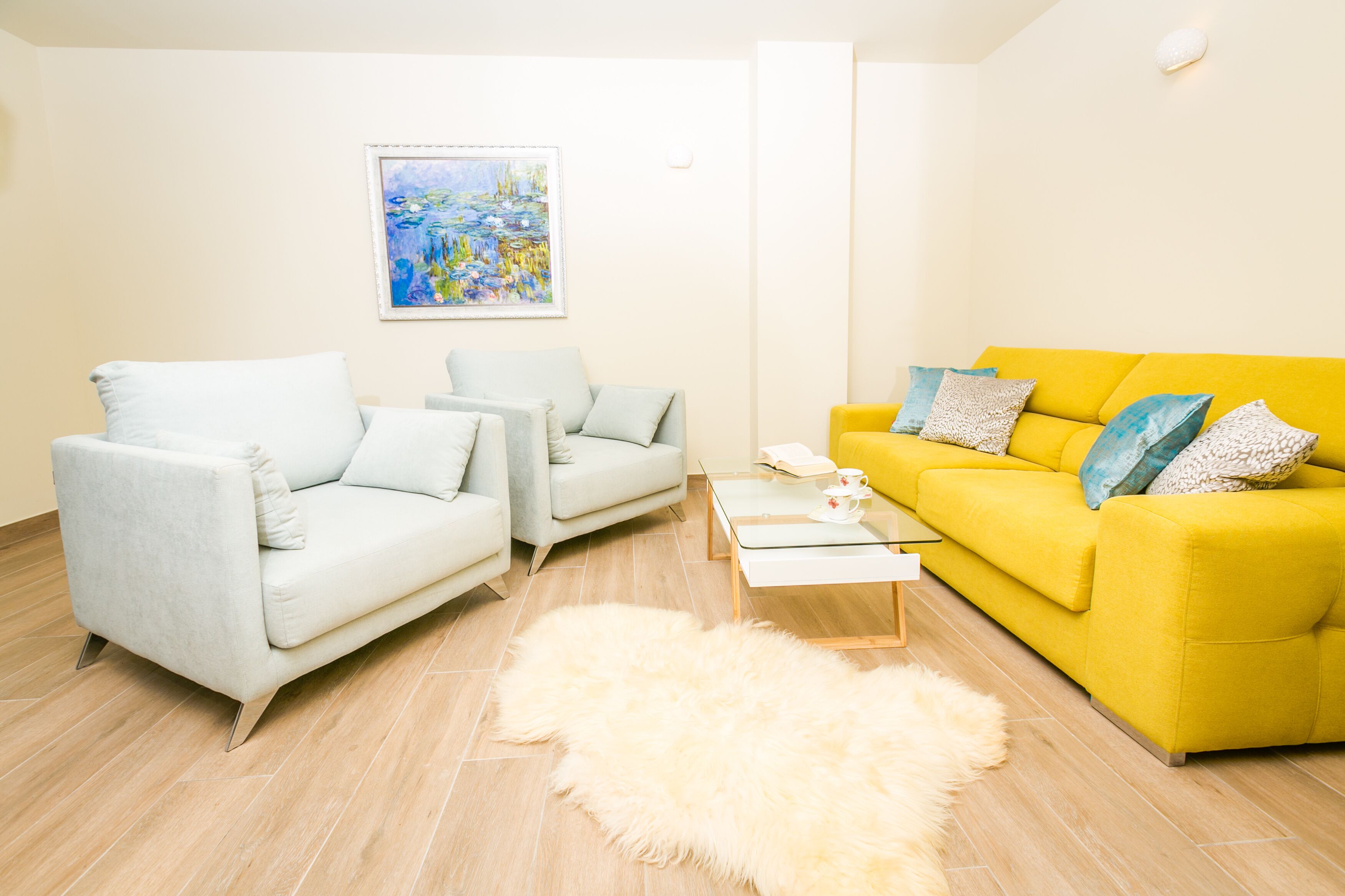 Un salon avec un canapé blanc, un canapé jaune et une table basse en verre.
