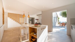 Une cuisine moderne dotée d’un îlot central, d’un escalier en bois et offrant une vue sur un patio extérieur.