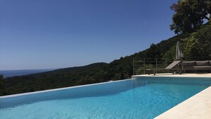 Une magnifique piscine à débordement d’un bleu profond, offrant une vue sur la mer et sur les collines environnantes.