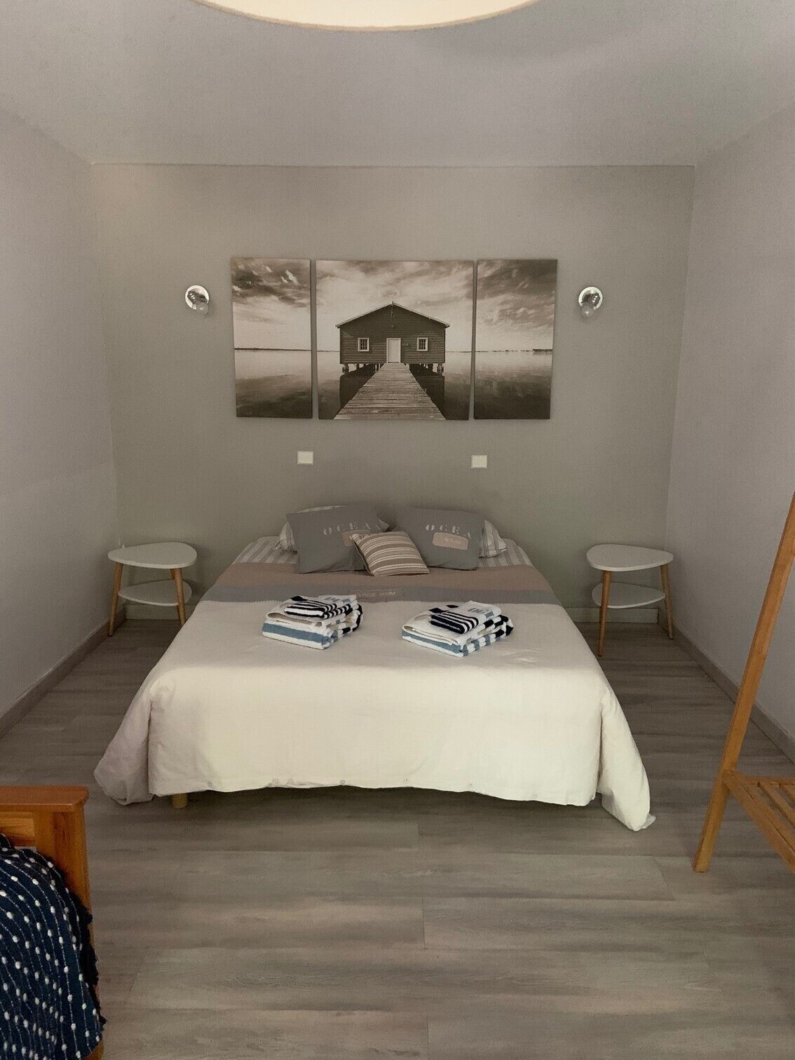 A bedroom with a bed, two bedside tables, a wooden floor, and a wall-mounted artwork of a house on a pier.