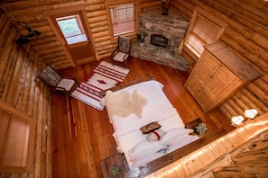A log cabin room with a bed, a stone fireplace, a window, and a chair.