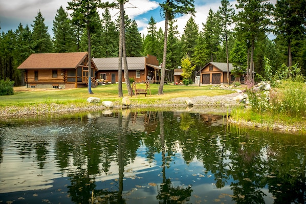 A cabin with a pond, surrounded by trees and a grassy area.