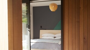 A modern bedroom with a bed, a hanging light fixture, and a view of the outdoors.