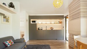 A modern living room with a grey sofa, a wooden dining table, and a kitchen area with grey cabinets and a microwave.