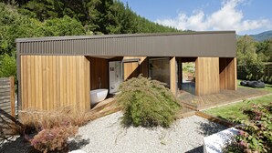 A modern cabin with a wooden exterior, a large window, and a visible bathroom.